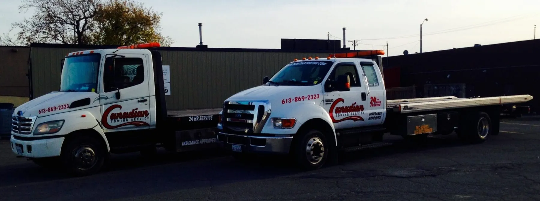 Two white tow trucks with Canadian Towing Service branding parked side by side in a lot, one with a flatbed trailer attached at the rear.